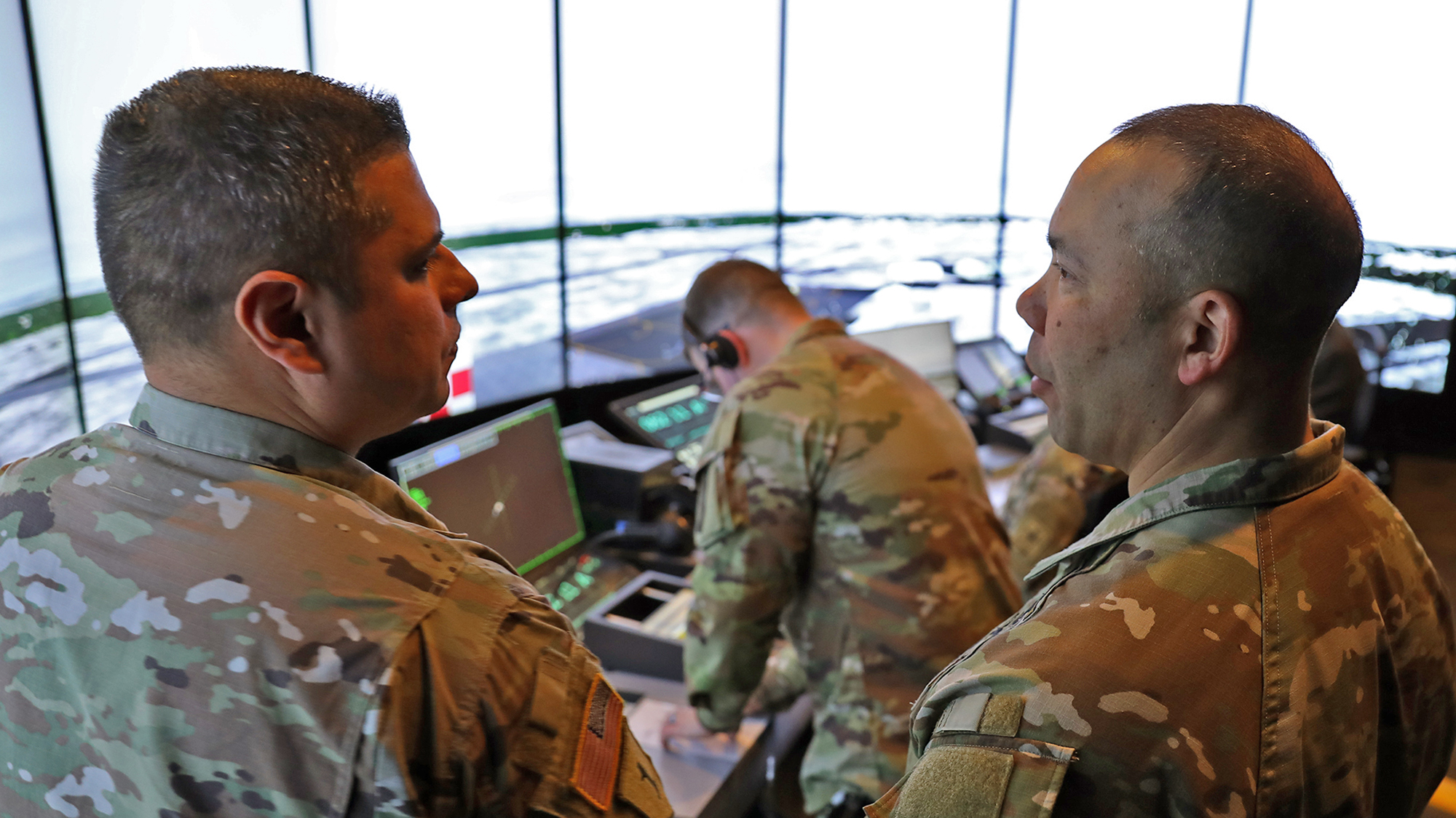 Two army soldiers examining a computer screen inside of a command and control center.