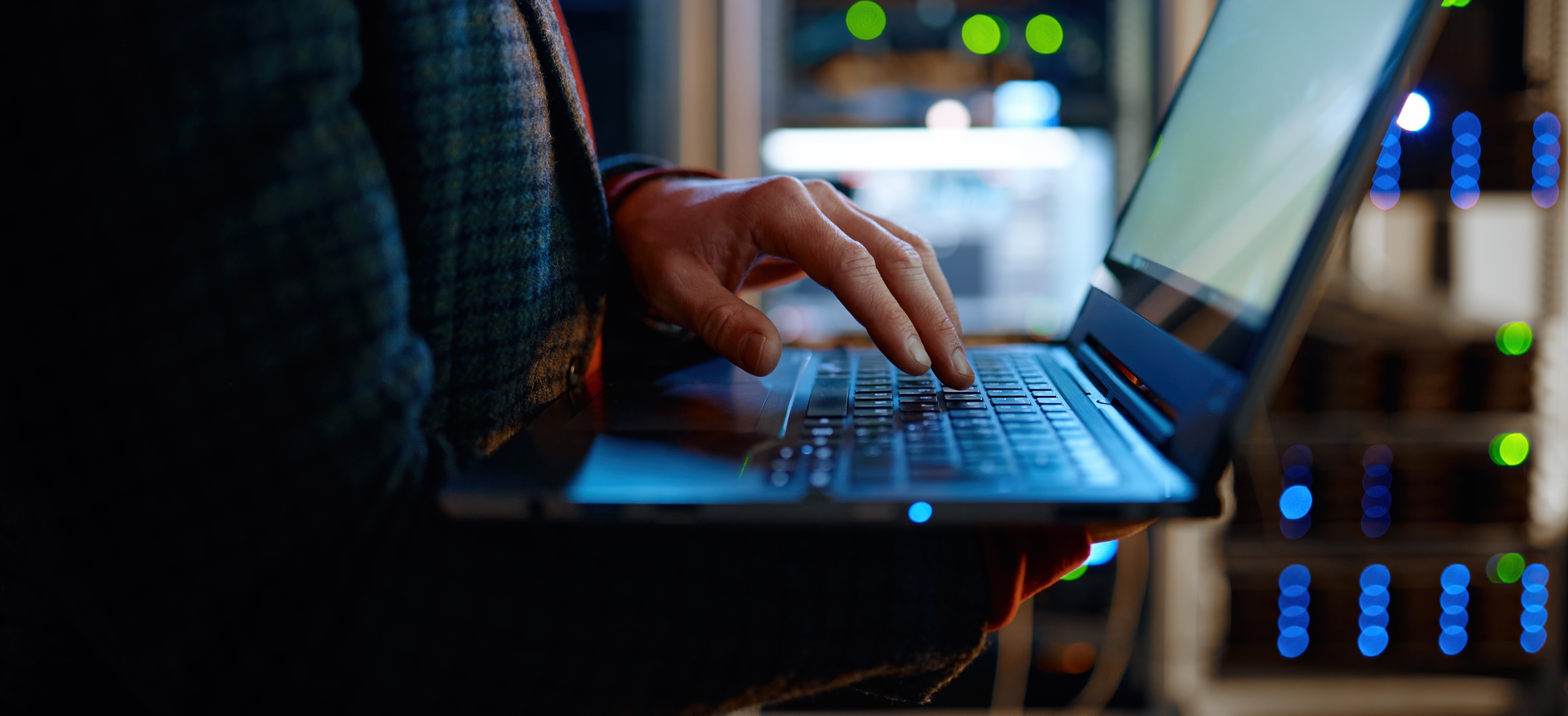 A person focused on typing on a laptop computer, with hands positioned on the keyboard and a screen illuminated.