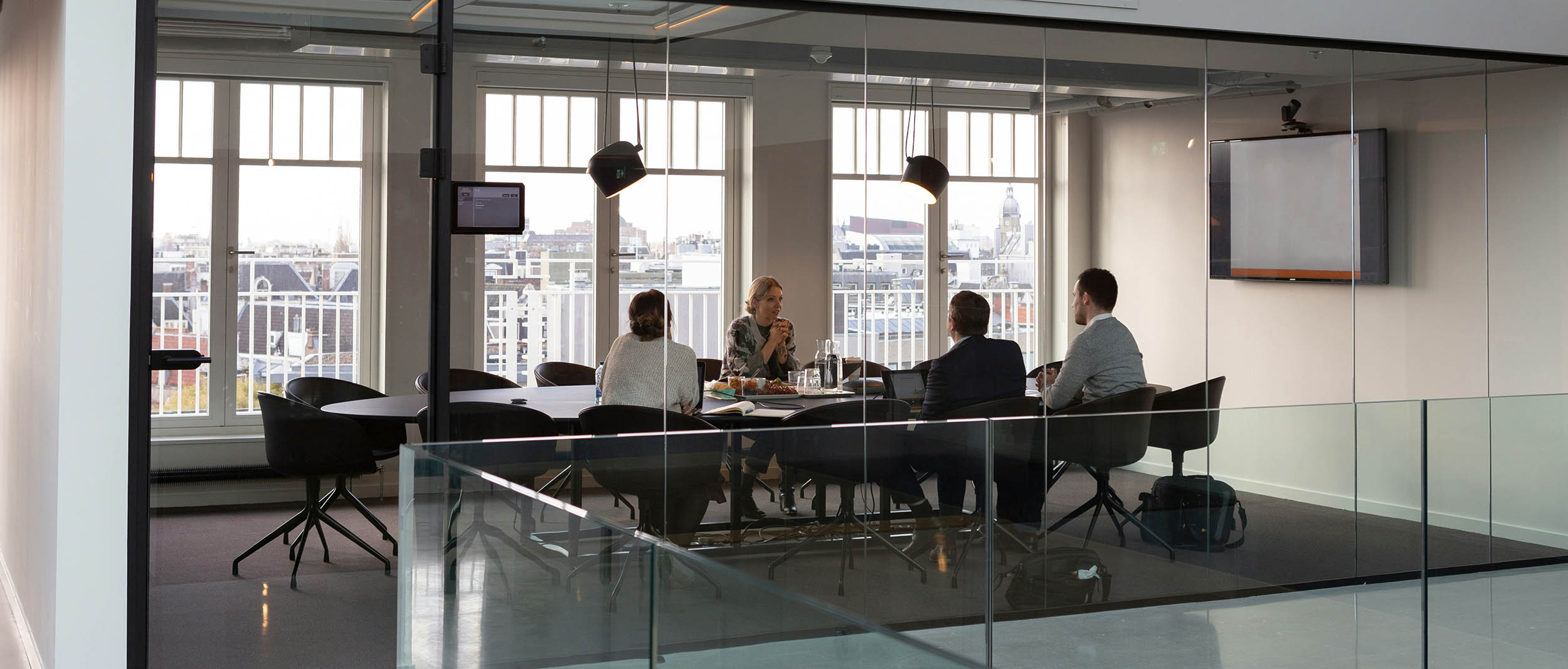 A glass-walled room featuring individuals seated around a table engaged in a meeting.