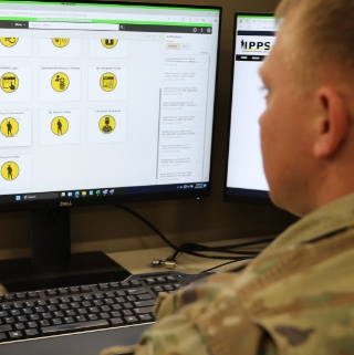 A soldier intently observes a computer screen displaying various yellow icons, highlighting a moment of focus and technology.