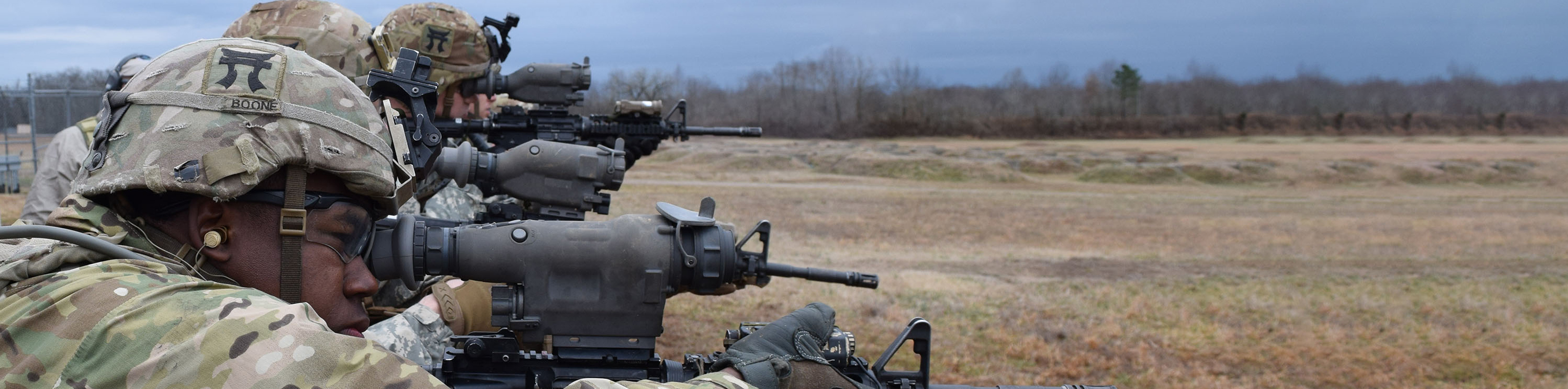 Soldiers stand in a field, holding rifles, ready for action amidst a natural landscape.