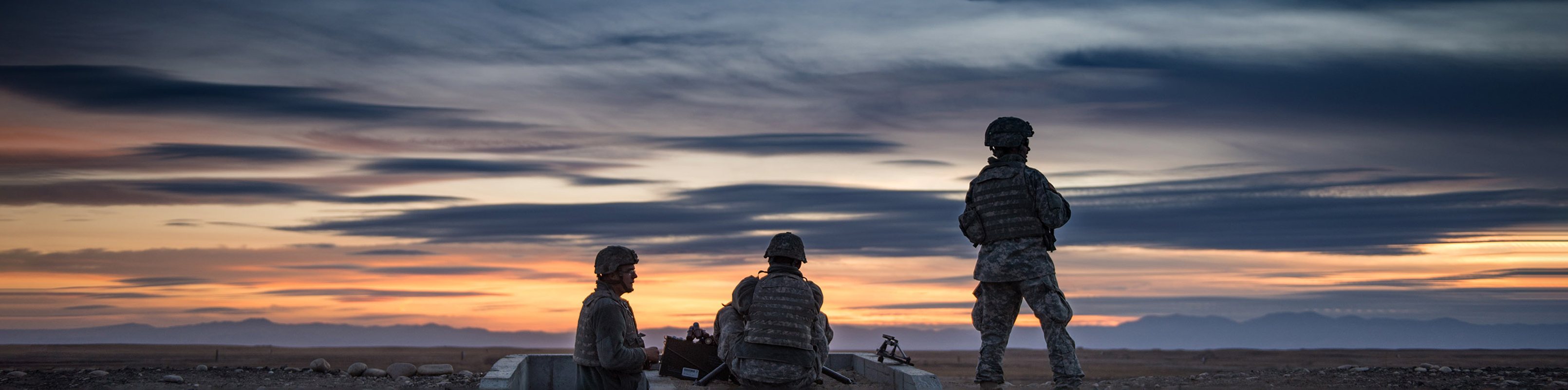 Three statues silhouetted against a vibrant sunset in a vast desert landscape.
