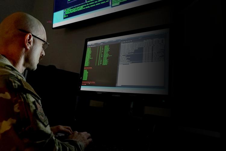 A soldier in uniform is seated at a desk, focused on a computer screen, engaged in a task or activity.